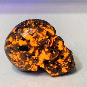 以下が含まれることがあります： 黒とオレンジのポリッシュされた石で作られた頭蓋骨。頭蓋骨は黒とオレンジのまだら模様をしています。