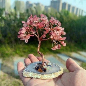 May include: A pink crystal tree with copper wire branches, standing on a grey agate slice base. The tree is decorated with small crystals of various colours.