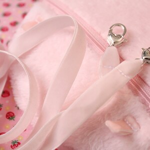 May include: A pink plush bag with a zipper closure and a pink satin strap with silver heart-shaped clasps.