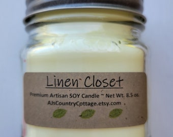 May include: A clear glass jar candle with a silver lid. The candle is labeled "Linen Closet" and is a premium artisan soy candle with a net weight of 8.5 ounces. The label also includes the website AJsCountryCottage.etsy.com.