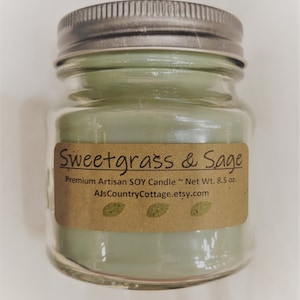 May include: A green glass jar candle with a silver lid. The label reads "Sweetgrass & Sage" and "Premium Artisan SOY Candle ~ Net Wt. 8.5 oz. AJsCountryCottage.etsy.com".