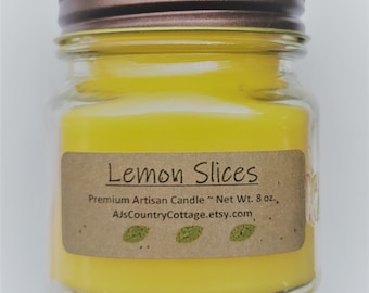 Puede incluir: Una vela amarilla en un tarro de vidrio con tapa marrón. La etiqueta dice "Lemon Slices", "Premium Artisan Candle", "Net Wt. 8 oz.", y "AjsCountryCottage.etsy.com".
