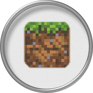 May include: A circular, silver-colored button with a pixelated image of a block of dirt with grass on top. The dirt block is brown with orange and light brown accents. The grass is green.