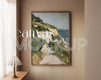 May include: A framed canvas mockup with a landscape painting, featuring a coastal scene with a path, cliffs, and sea. The text "canvas MOCKUP" is overlaid on the image. A lamp and small objects sit on a wooden ledge. The image also includes the text "4K RESOLUTION 300DPI".