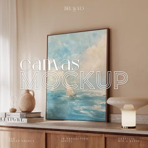 以下が含まれることがあります： 青い海に浮かぶヨットを描いた海景画のフレーム付きキャンバスモックアップ。雲の多い空の下。画像には「canvas MOCKUP」の文字が重ねられています。木製のキャビネットには、ランプ、花瓶、本が置かれています。