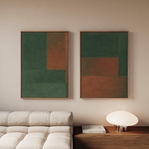 May include: Two framed abstract artworks. Each features a geometric design with green and rust-coloured blocks. The frames are a light brown colour. The artworks are displayed above a light-coloured sofa and a wooden cabinet.