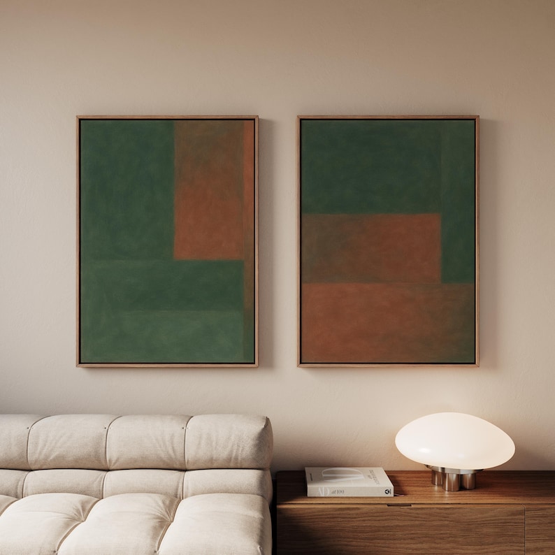 May include: Two framed abstract artworks. Each features a geometric design with green and rust-coloured blocks. The frames are a light brown colour. The artworks are displayed above a light-coloured sofa and a wooden cabinet.
