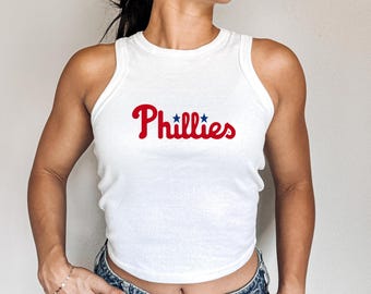 Op de afbeelding: Een wit tanktop met een rood "Phillies" logo met blauwe sterren.