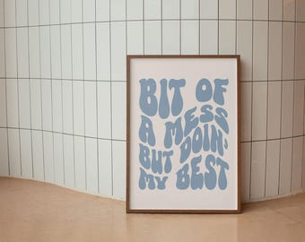 May include: A framed print with the text "Bit of a mess but doing my best" in light blue, stylized lettering. The print has a white background and a brown frame. The artwork is displayed against a white tiled wall.