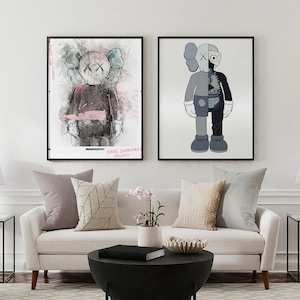 Peut inclure: Deux impressions d'art encadrées d'un personnage de dessin animé avec des yeux en forme de X noirs. Le personnage de gauche est dans un style aquarelle et le personnage de droite est dans un style plus graphique. Les impressions sont accrochées à un mur blanc au-dessus d'un canapé blanc avec des coussins.