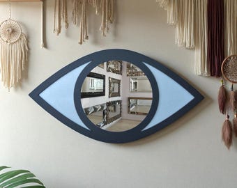 Könnte beinhalten: Ein augenförmiger Wandspiegel mit dunkelblauem Rahmen und hellblauer Iris. Der Spiegel reflektiert einen Raum mit mehreren gerahmten Spiegeln. Dekorative Makramee-Wandbehänge und ein Traumfänger sind im Hintergrund zu sehen.