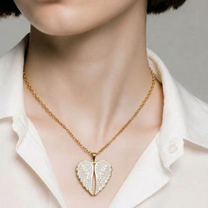 Puede incluir: Un collar dorado con un colgante en forma de alas de &aacute;ngel. Las alas est&aacute;n adornadas con peque&ntilde;os cristales brillantes. El collar se lleva sobre una camisa blanca.