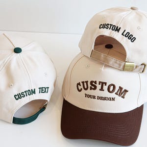 Puede incluir: Tres gorras de béisbol personalizadas en crema, marrón y verde. Una gorra tiene una visera verde y el texto "CUSTOM TEXT". Otra tiene una visera marrón con "CUSTOM YOUR DESIGN". La tercera gorra tiene "CUSTOM LOGO" en la parte trasera.