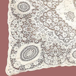 May include: Ivory lace tablecloth with detailed floral and geometric patterns. The lace has a scalloped edge. The tablecloth is a vintage style, suitable for special occasions or home decor.