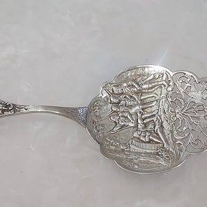 May include: Silver cake server with an ornate handle and a decorative blade. The blade features a detailed relief scene and openwork floral patterns. The handle has intricate floral and scroll designs.