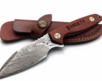 May include: A Damascus steel blade knife with a wooden handle engraved with the name "ROBERTO". The knife is accompanied by a brown leather sheath with a decorative emblem and stitching. The knife has a full tang construction.