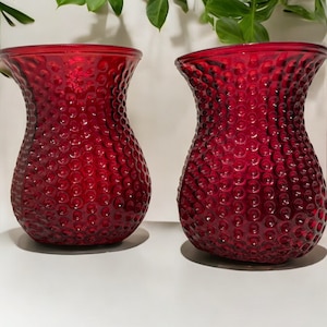 May include: Two red glass vases with a textured, bubble-like surface. The vases are round and have a wide opening at the top.