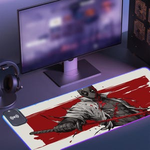 May include: A white and red gaming mouse pad with a black and white illustration of a character with a red sword. The mouse pad has a blue glow around the edges and a wireless charging pad in the corner.
