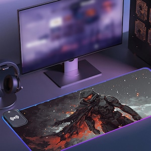 May include: A black and gray gaming mouse pad with a blue glow around the edges. The mouse pad features a digital illustration of a futuristic soldier in a black and gray suit with a red and orange glow around the figure. The mouse pad has a wireless charging pad in the top left corner.