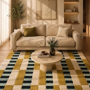 May include: A modern living room featuring a beige sofa with olive and cream-colored throw pillows. A round, light-colored coffee table sits on a geometric rug with mustard yellow, black, and cream rectangular patterns. The room has a neutral color palette.