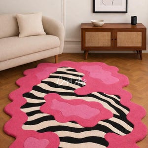 Turn your floor into a piece of art with this bold hand-tufted zebra print rug accented by vibrant pink pops and an irregular, wavy edge. This rug combines contemporary style with playful energy, making it the perfect centerpiece for modern, eclectic, or creative interiors. Whether in your living room, bedroom, or studio space, this rug adds an instant splash of personality while providing cozy comfort underfoot.
