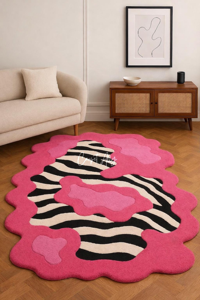 Turn your floor into a piece of art with this bold hand-tufted zebra print rug accented by vibrant pink pops and an irregular, wavy edge. This rug combines contemporary style with playful energy, making it the perfect centerpiece for modern, eclectic, or creative interiors. Whether in your living room, bedroom, or studio space, this rug adds an instant splash of personality while providing cozy comfort underfoot.