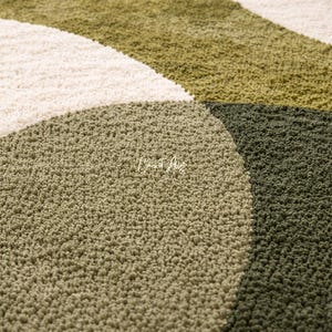 Hand tufted abstract area rug in olive green and ivory with organic curved design placed in a modern living room. Soft textured rug with nature inspired pattern and neutral tones, ideal for contemporary home décor, minimalist interiors, and living room styling.