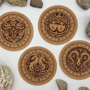 Könnte beinhalten: Vier Korkuntersetzer mit eingravierten Sternzeichen. Die Zeichen sind Stier, Zwillinge, Krebs und Löwe. Die Untersetzer sind rund und haben eine braune Korkoberfläche.