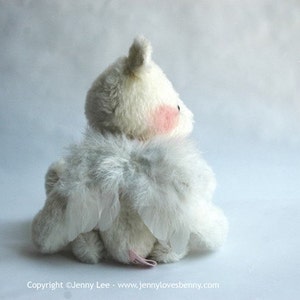 May include: A white plush toy with feathery wings. The toy is sitting on a white surface and is looking to the right.