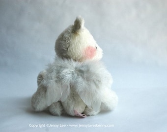 May include: A white plush toy with feathery wings. The toy is sitting on a white surface and is looking to the right.