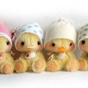 May include: Four plush yellow ducklings wearing different patterned fabric hats. The ducklings are sitting on a white surface.