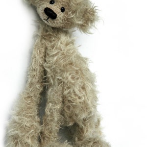 Pode incluir: Um urso de peluche bege com pelo longo e felpudo e olhos pretos. O urso está em pé sobre um fundo branco.