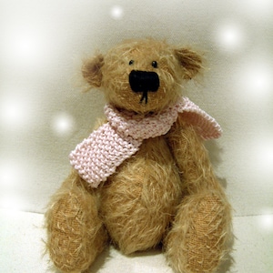 May include: A brown teddy bear wearing a pink knitted scarf. The bear has a black nose and eyes. The background is a white, blurry surface.