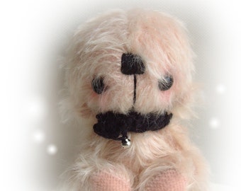 May include: A small, pink, furry teddy bear with black eyes and a black bow tie. The bear is sitting on a white surface.