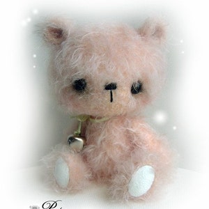 May include: A soft, pink, fuzzy teddy bear with a bell around its neck. The bear has black eyes and a black nose. The bear is sitting on a white surface.