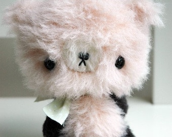 May include: A pink fluffy teddy bear with black eyes and a black nose. The bear is wearing a light green scarf and has black paws.