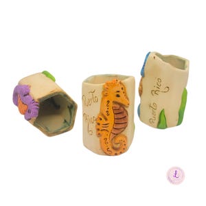 May include: Three ceramic shot glasses with a beige base. One glass features a seahorse design in orange and brown, and the words "Puerto Rico". The other two glasses have colorful accents and the words "Puerto Rico".