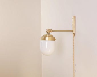 May include: A brass wall sconce with a white glass globe shade. The sconce has a pivoting arm and a decorative cord. The fixture is mounted on a light-colored wall, providing a warm, ambient light source.