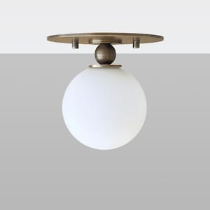 May include: A ceiling light fitting with a round, white glass shade and a brass base. The base has a small, round wooden knob.