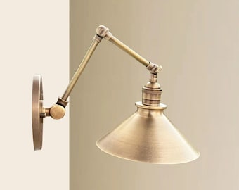 May include: A brass wall-mounted light fixture with a swivel arm and a cone-shaped shade. The light fixture has a vintage industrial style.