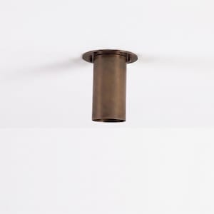 May include: A bronze-coloured ceiling light fitting. The fitting has a circular base and a cylindrical body. The light is designed to be recessed into the ceiling. The fitting is made of metal and has a smooth finish.