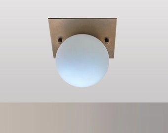 May include: A modern ceiling light fixture with a square brass base and a frosted glass globe.