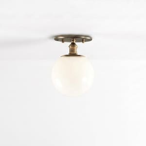 May include: A semi-flush mount ceiling light fixture featuring a spherical white glass globe shade attached to a circular antique brass finish metal canopy. The fixture has a short, cylindrical stem connecting the globe to the ceiling mount.