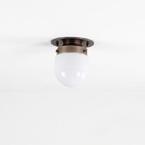 May include: A ceiling light fixture with a bronze-colored base and a white, oval-shaped glass shade. The fixture is mounted on a white ceiling. The light has a vintage or industrial design.