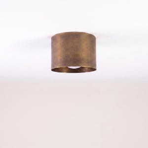 May include: A cylindrical ceiling light fitting with a bronze finish. The light is mounted directly to the ceiling and has a single bulb visible at the bottom. The fitting is a simple, modern design.