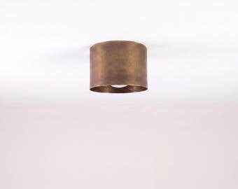 May include: A cylindrical ceiling light fixture with a bronze finish. The light is mounted directly to the ceiling and has a single bulb visible at the bottom. The fixture is a simple, modern design.