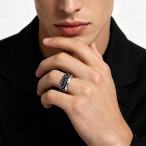 May include: A silver ring featuring a wide band with a textured, black, grid-like pattern across the center. The ring has smooth, polished silver edges on both the top and bottom, creating a distinct contrast against the dark, recessed inlay.