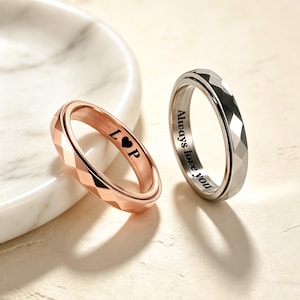 May include: Two metal rings with faceted outer surfaces. One ring is rose gold-toned and engraved with the letters L, a heart symbol, and P. The other ring is silver-toned and engraved with the text Always love you on the inner band surface.
