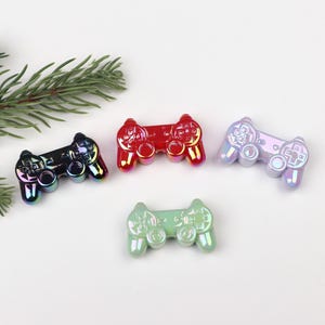 May include: Four iridescent plastic game controllers in different colours: black, red, green, and purple. The controllers are shaped like a traditional video game controller with buttons and a directional pad.