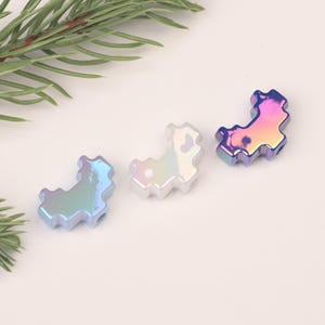 Op de afbeelding: Drie regenboogkleurige plastic kralen in de vorm van een halve maan. De kralen zijn in de kleuren blauw, wit en roze.